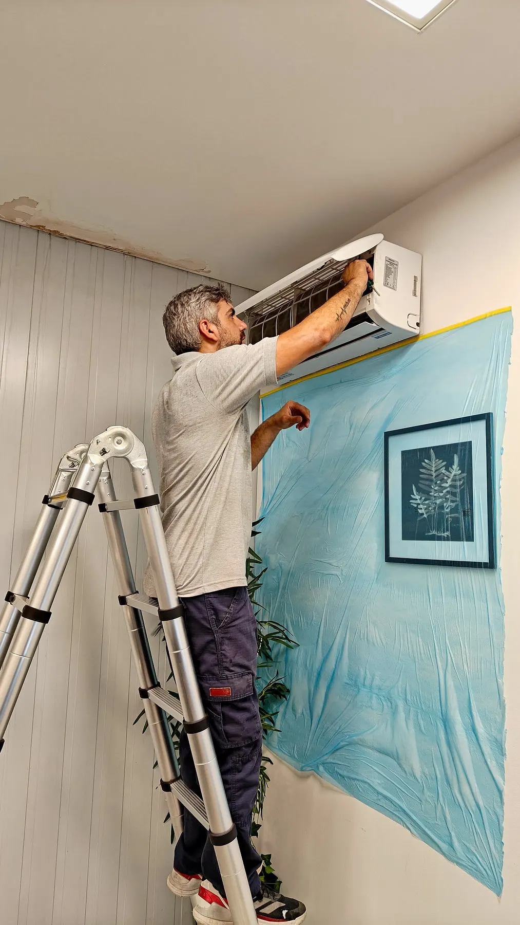 Técnico limpiando un split en altura con la pared protegida